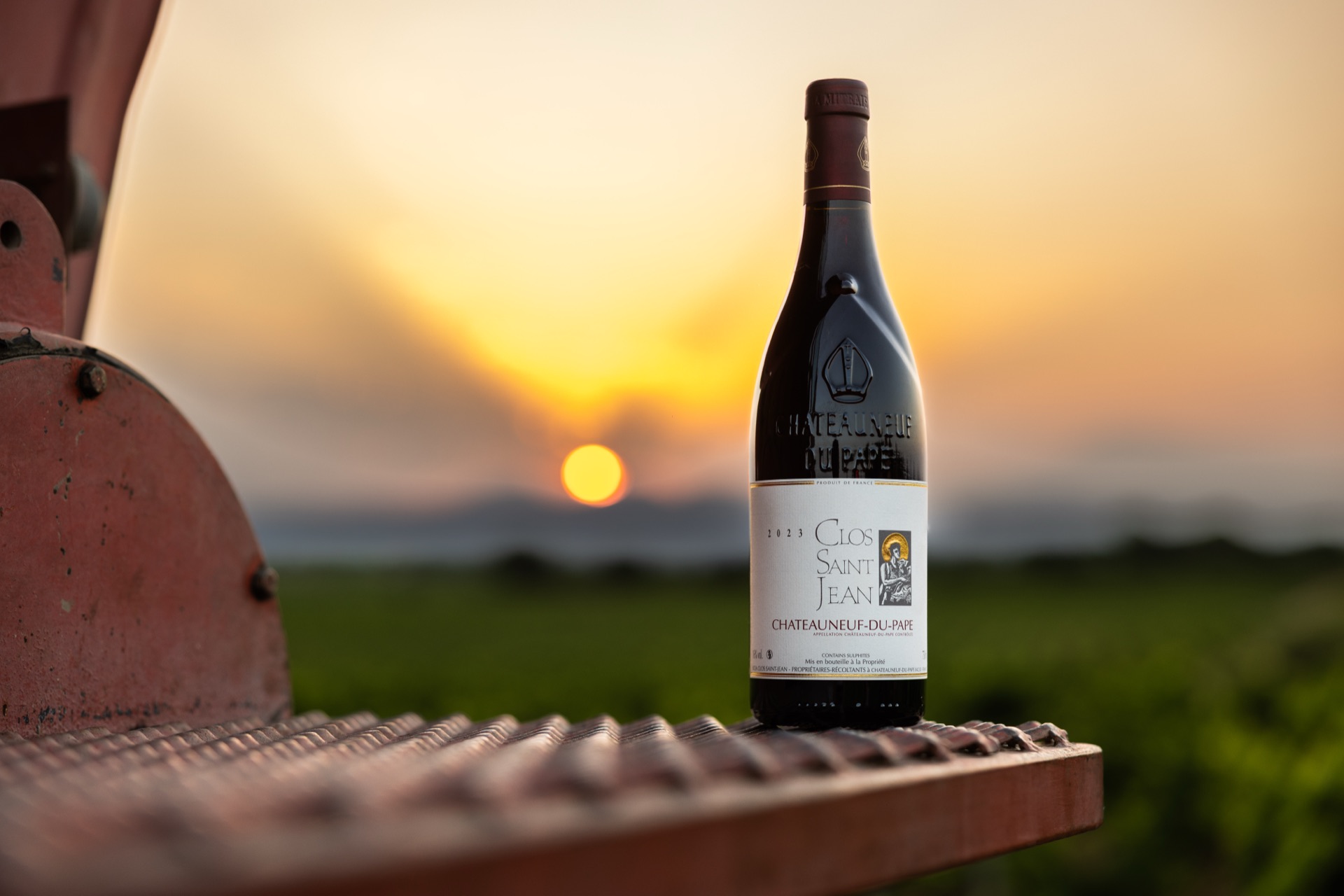 A bottle of Clos Saint Jean stood on the tractor's grille as the sun comes up over the vines
