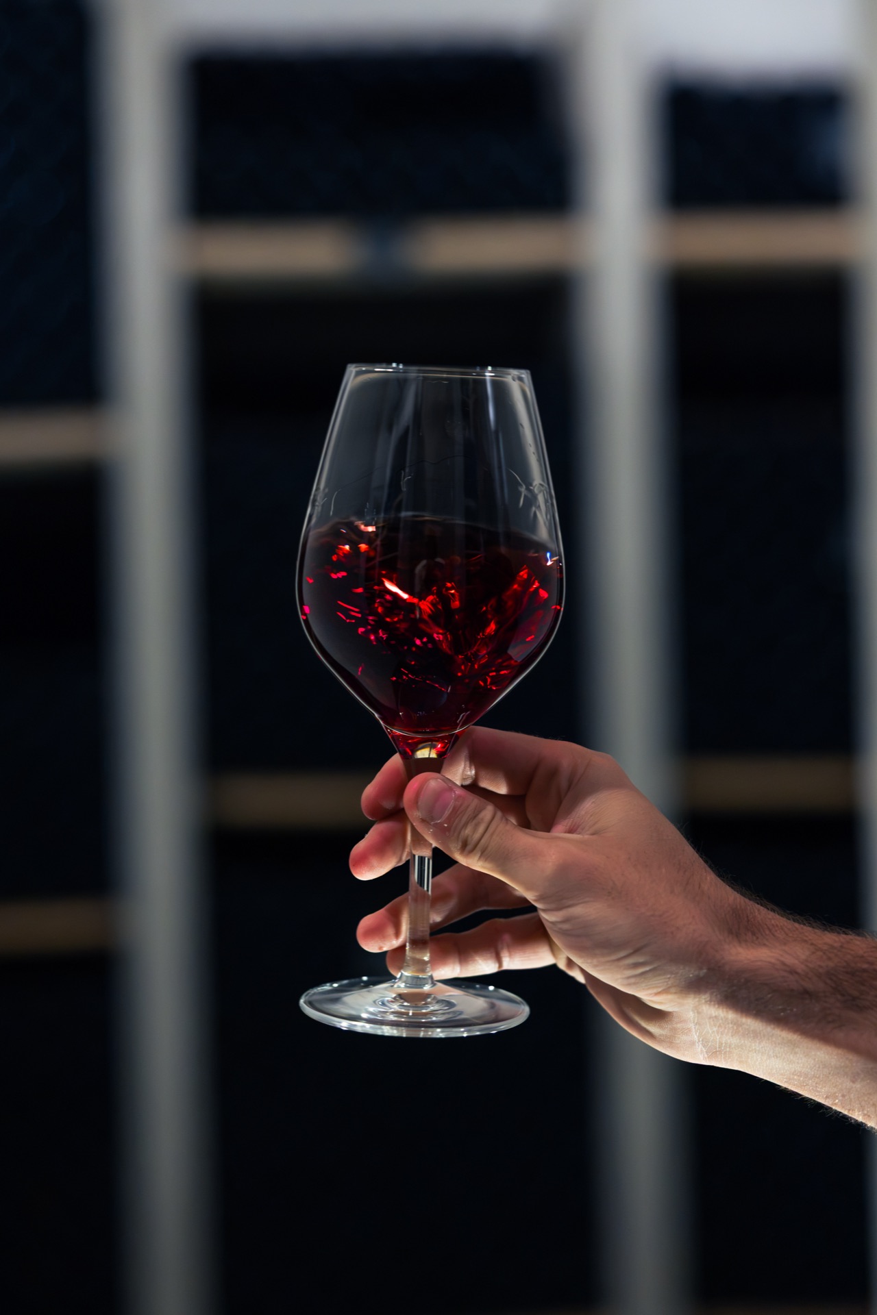 A glass of red held up against the racked bottles