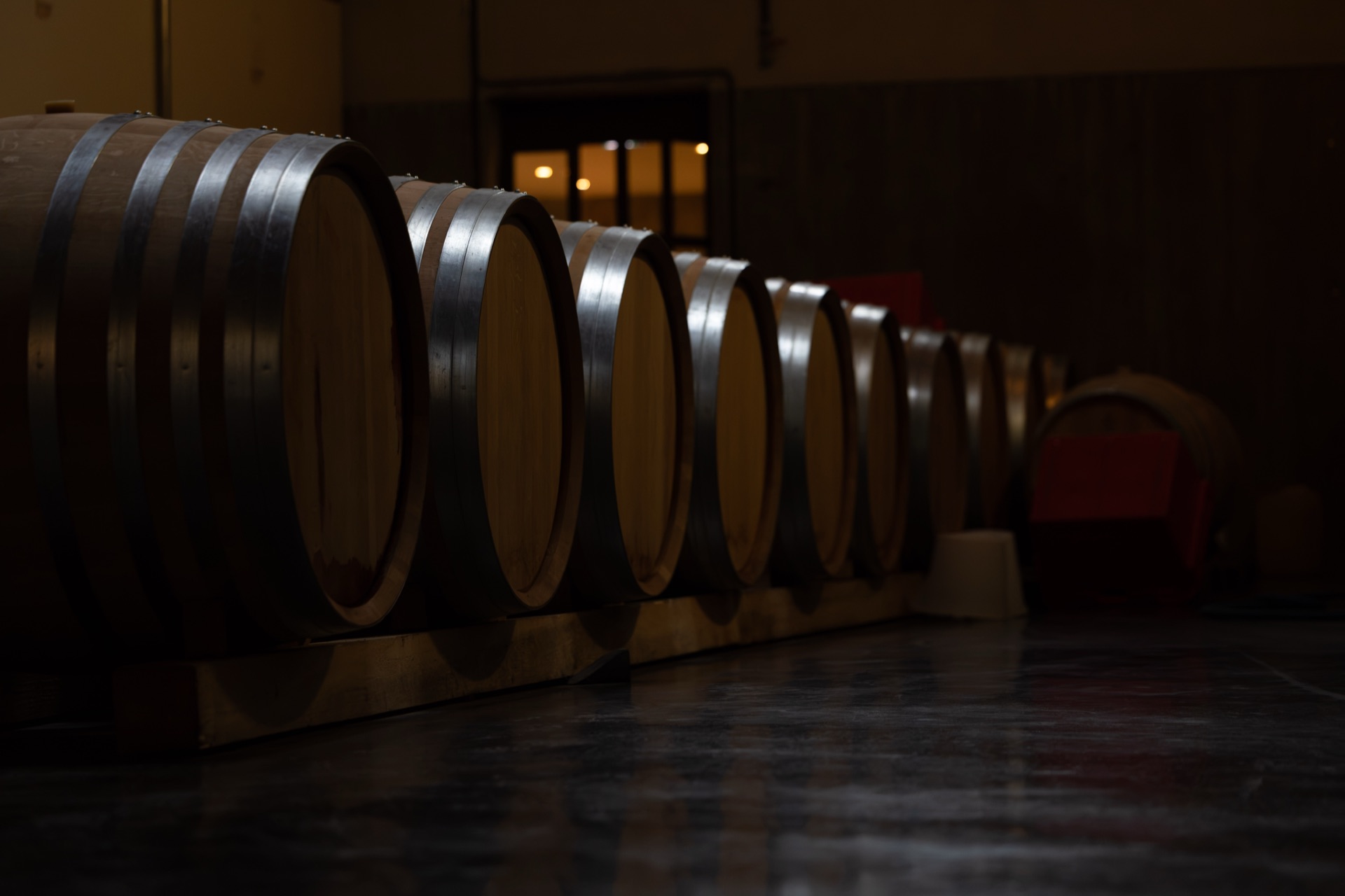 The barrel row receding into the dark, a lit doorway at the far end