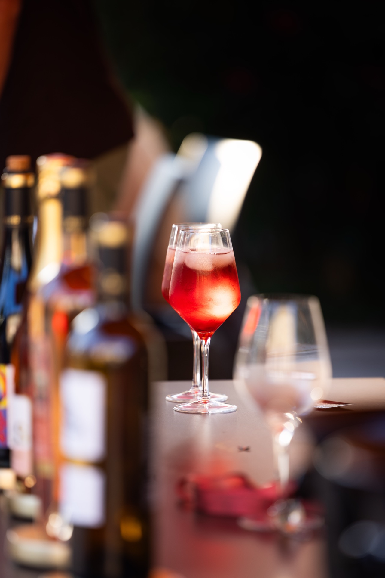 A filled glass on the bar top, bottles falling out of focus behind