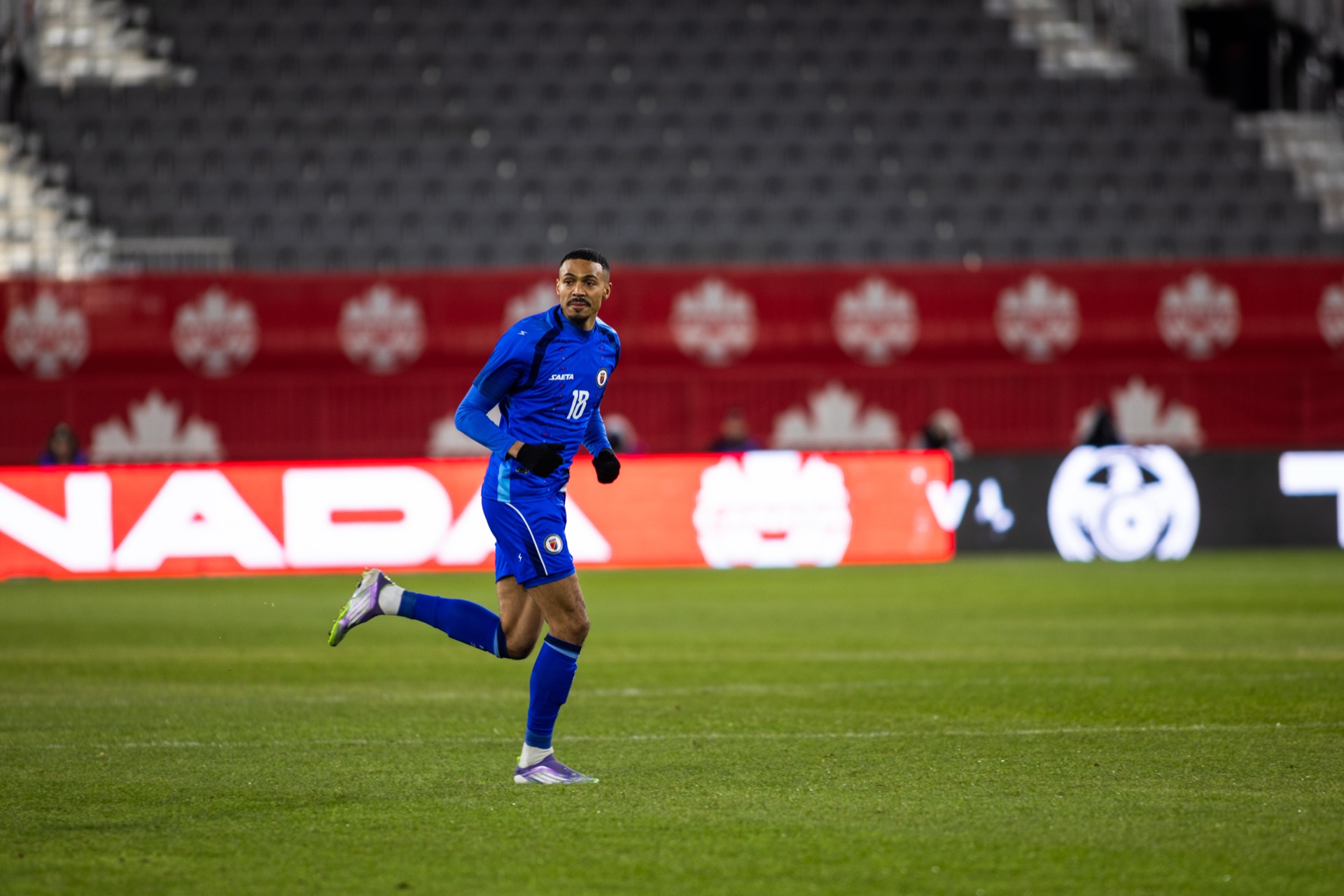 Wilson Isidor jogging across an empty pitch in Haiti's blue kit, number 18, before the stands filled