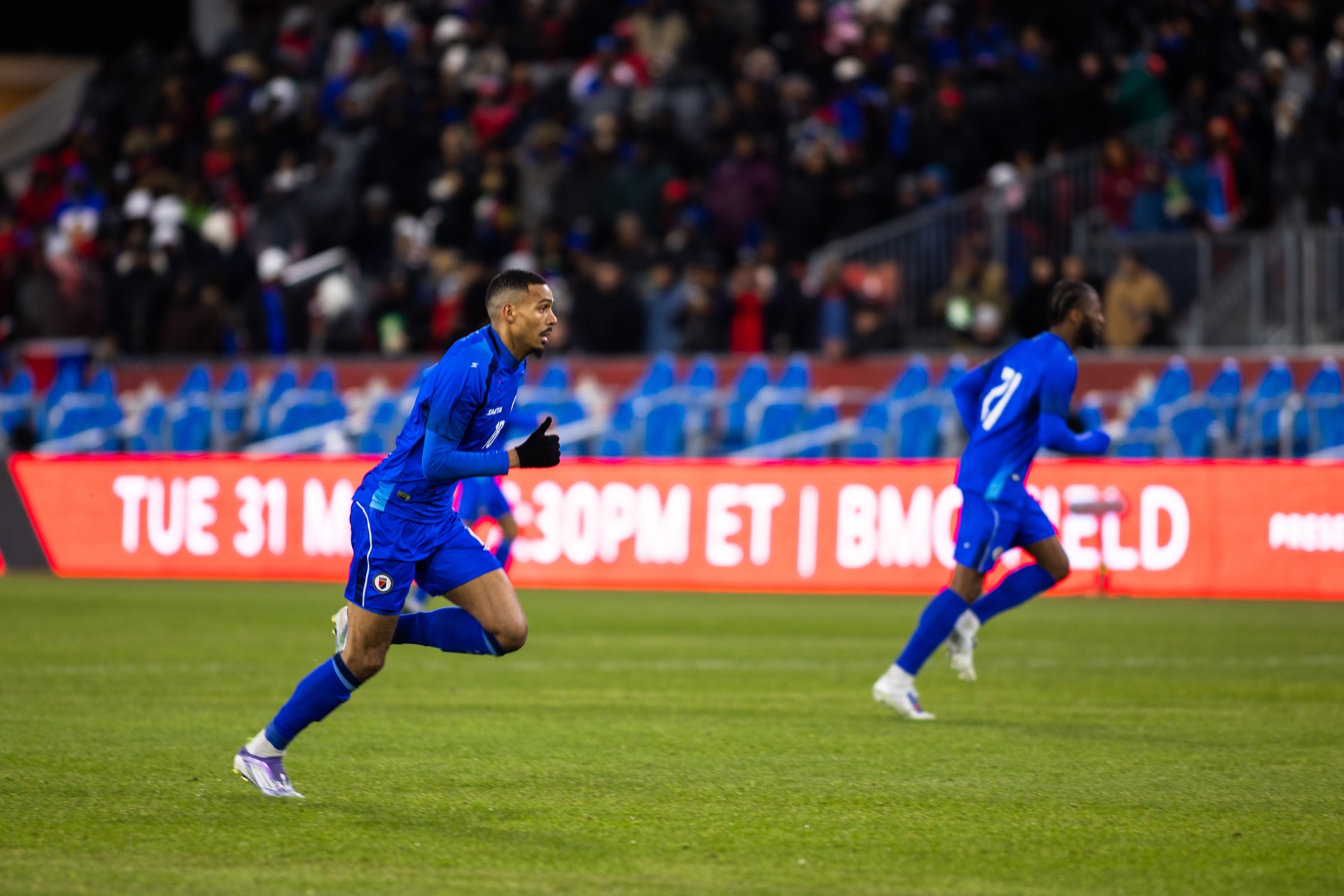 Isidor at a run past a teammate, the LED hoarding behind him reading BMO FIELD