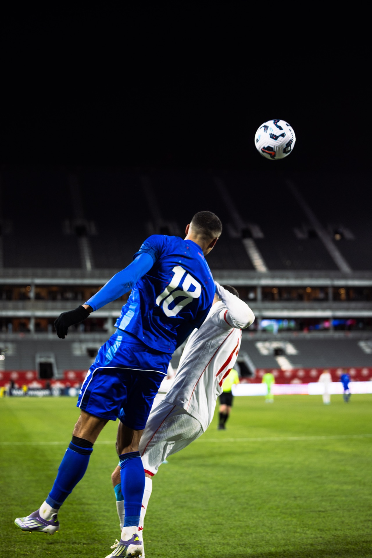 Isidor rising into an aerial challenge with a Tunisia defender, the ball hanging above them against a dark empty stand
