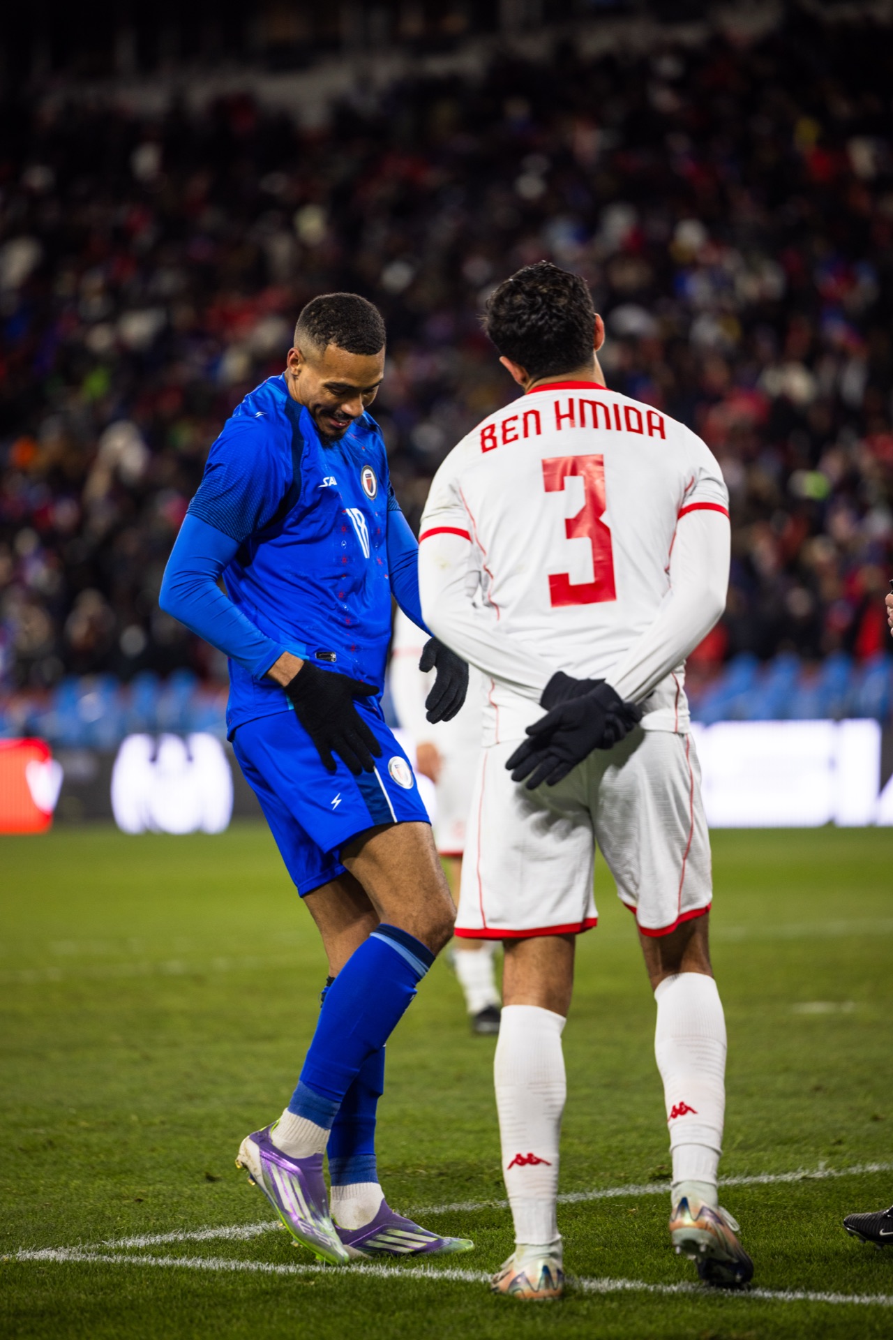 Isidor and Tunisia's number 3 side by side on the touchline, both heads down and laughing