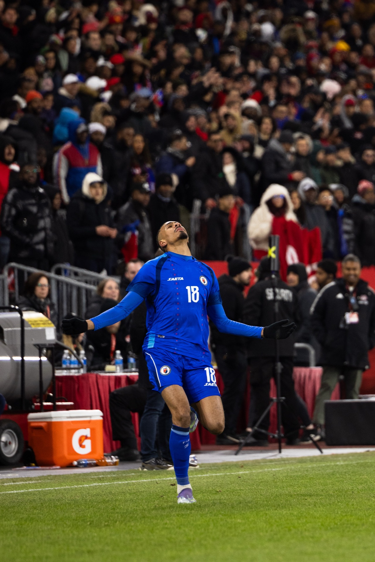 Isidor with his head tipped back and arms open, breath showing, the crowd and the team benches behind him