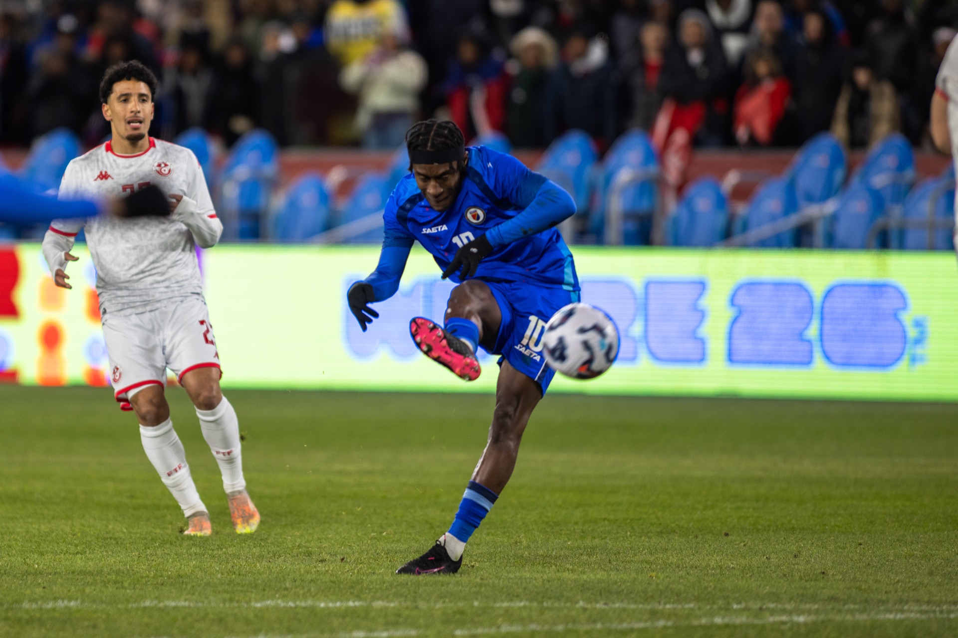 Haiti's number 10 hitting the ball on the half-volley as a Tunisia player turns away from it