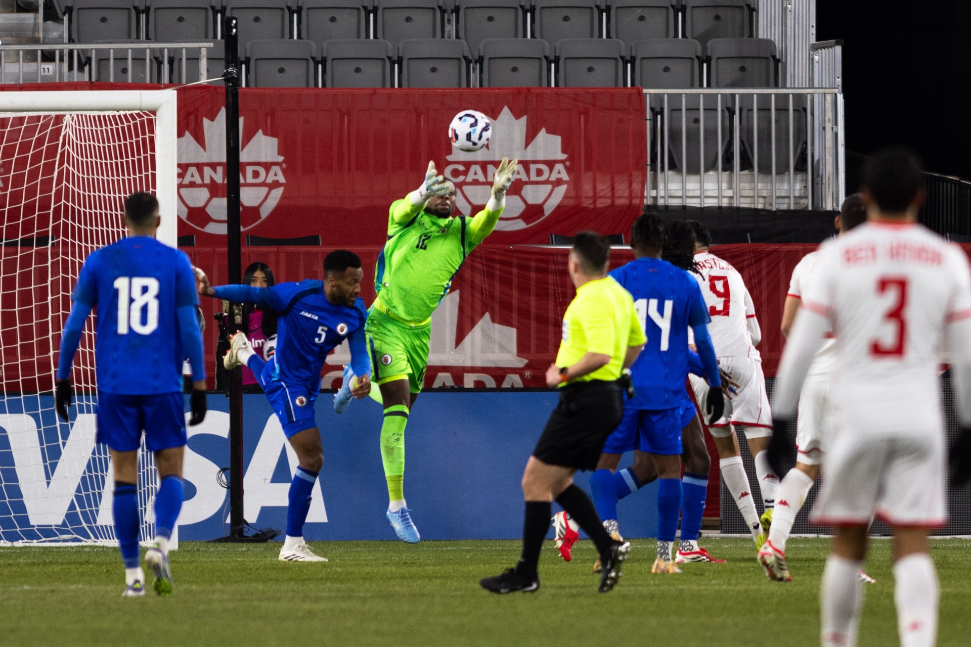 Haiti's goalkeeper in green at full stretch punching the ball clear at the near post, defenders and the referee watching it go