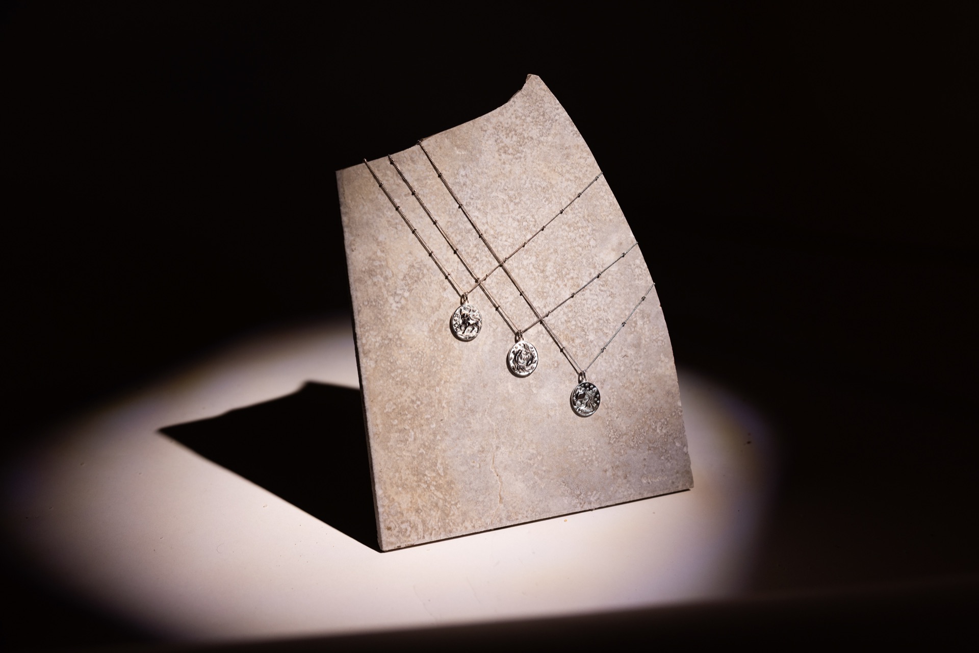 Silver pendants on a stone display block, lit by a single hard spotlight in the dark