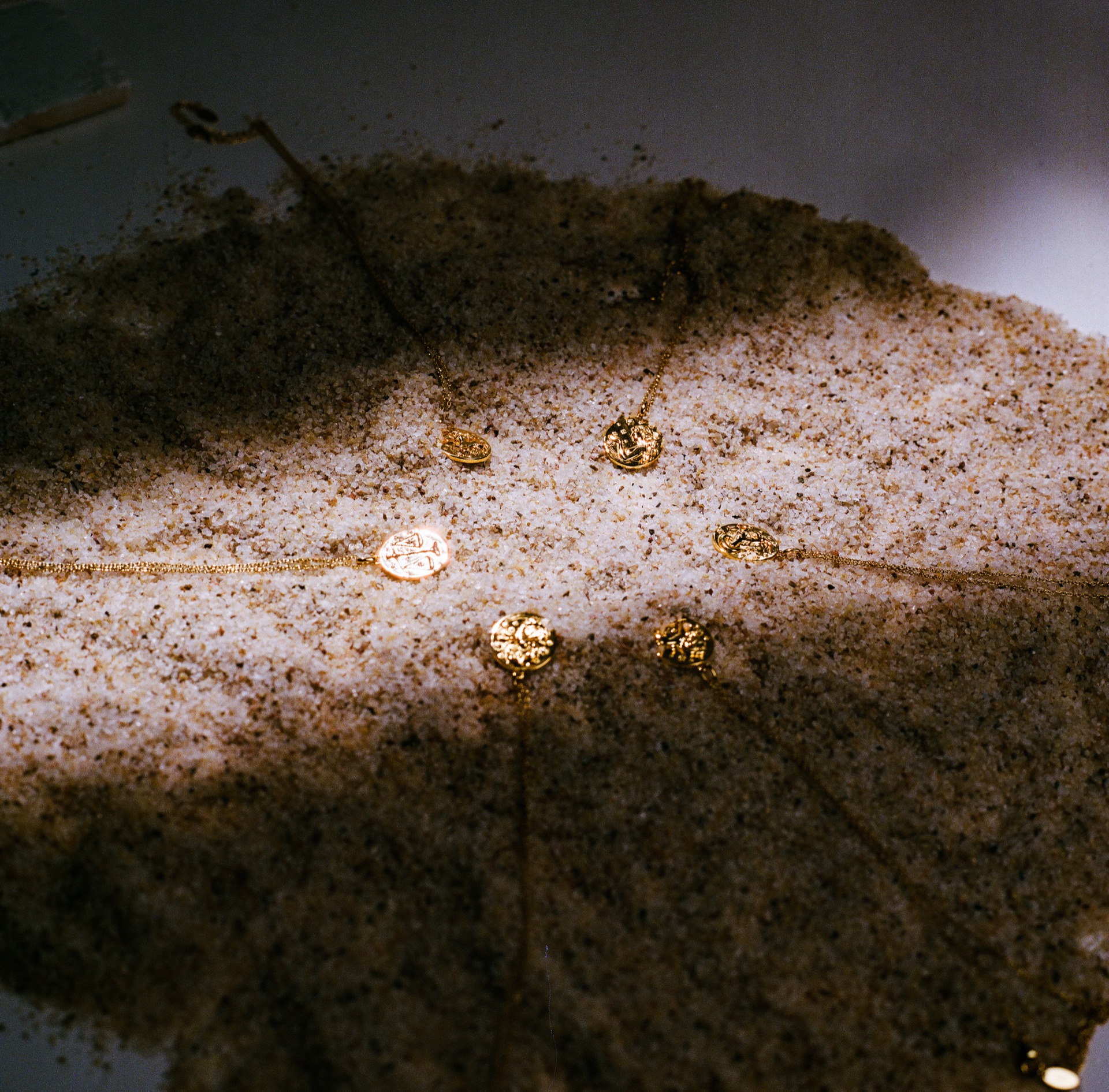 Gold and blackened zodiac pendants scattered across wet, rippled sand
