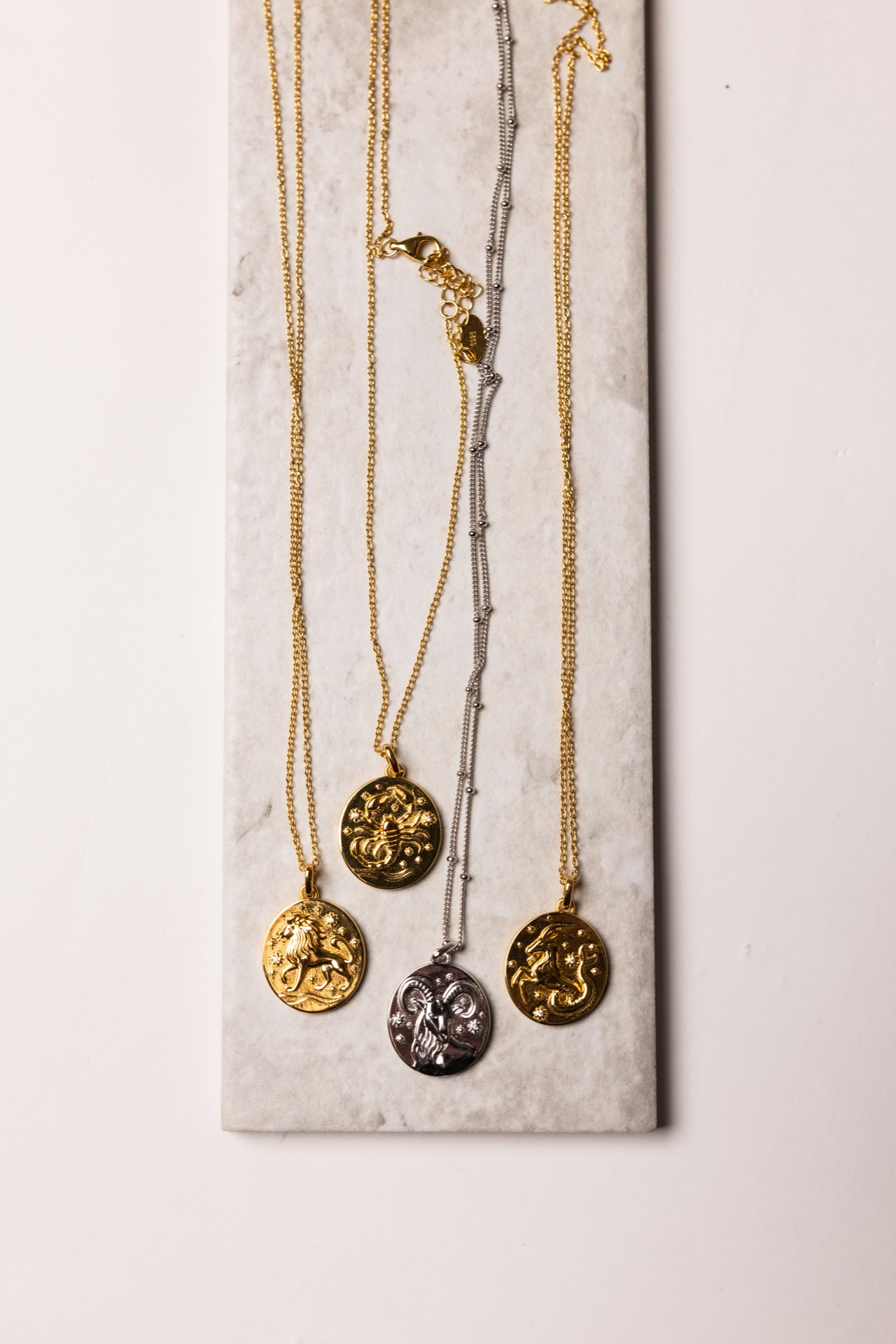 Gold and silver zodiac necklaces draped over a pale stone slab