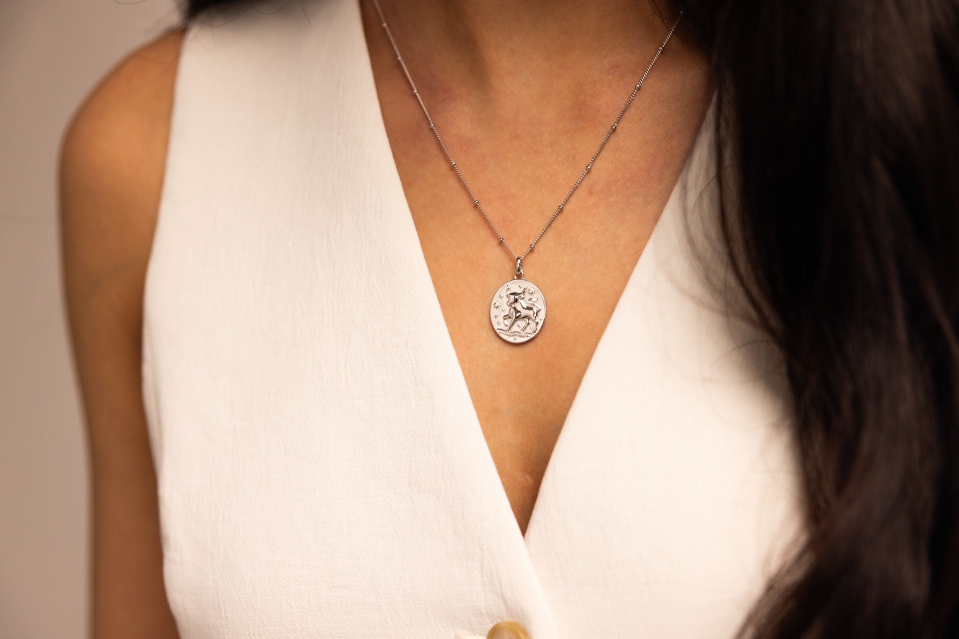 Silver zodiac pendant resting at the neckline of a white top