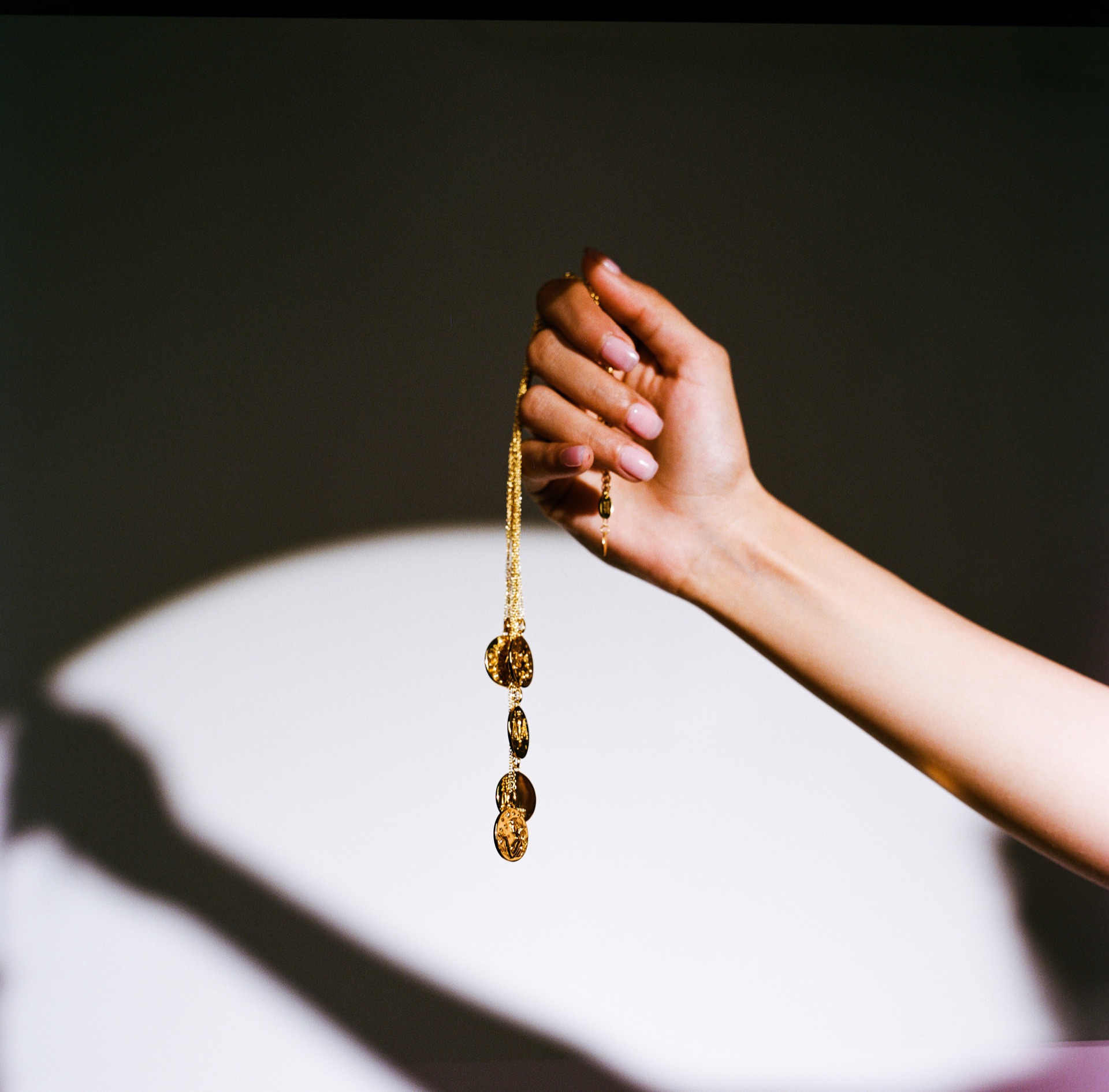 A hand holds a chain of gold pendants above a pool of hard light on a dark surface