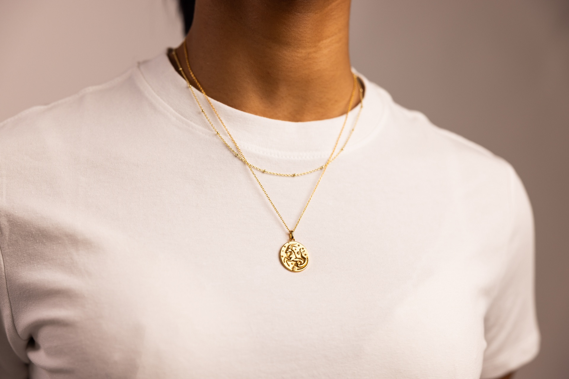 Three layered gold chains and a zodiac pendant worn over a plain white t-shirt