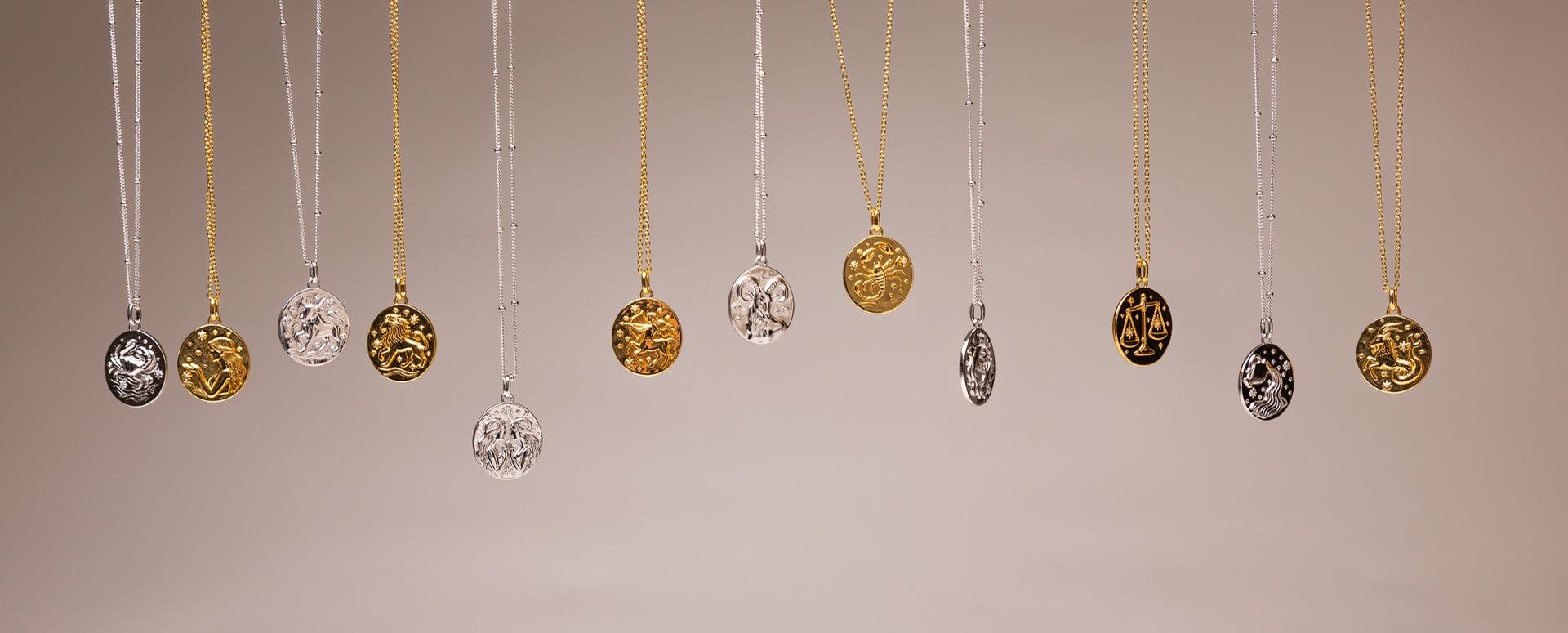 The full run of Sacred Haven pendants hung in one long row, gold and silver alternating against a pale wall