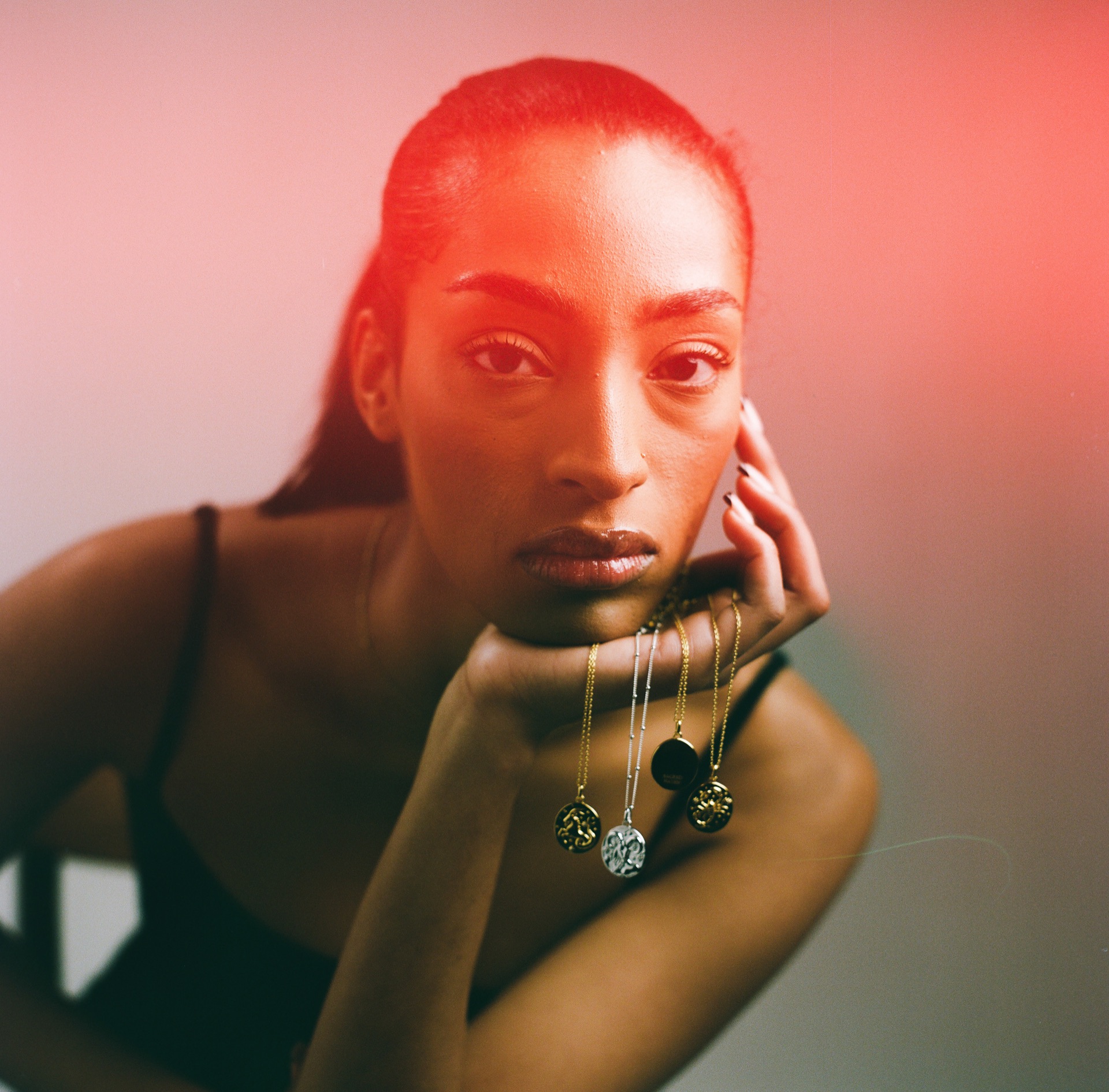 The same portrait lit with red and teal gels, the layered pendants picked out against the colour