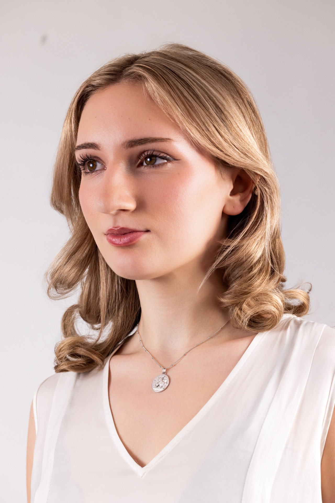 Blonde model in a white top against a pale backdrop, a silver zodiac pendant at her throat
