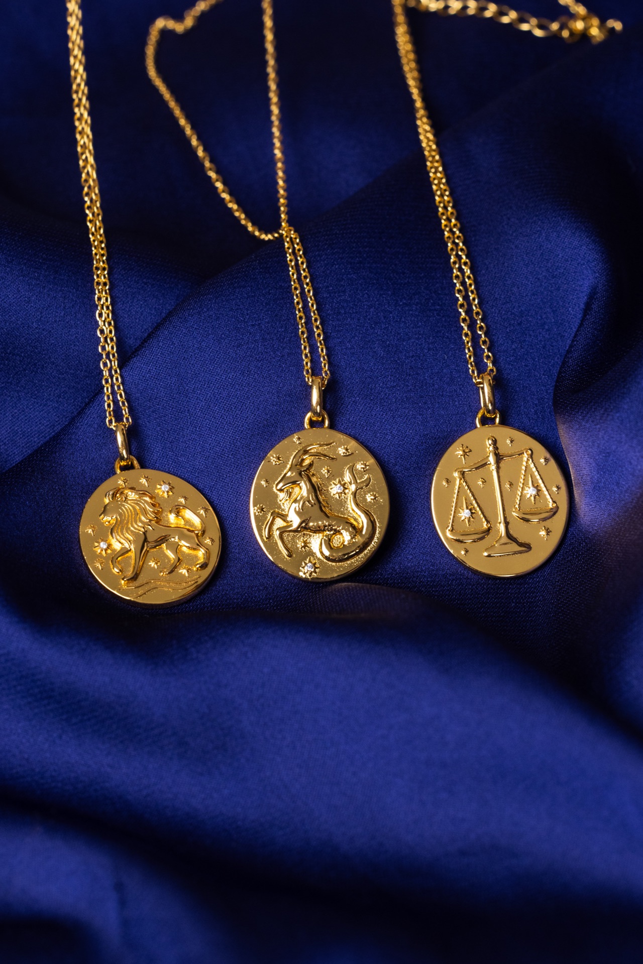 Three gold zodiac pendants arranged on folded blue satin