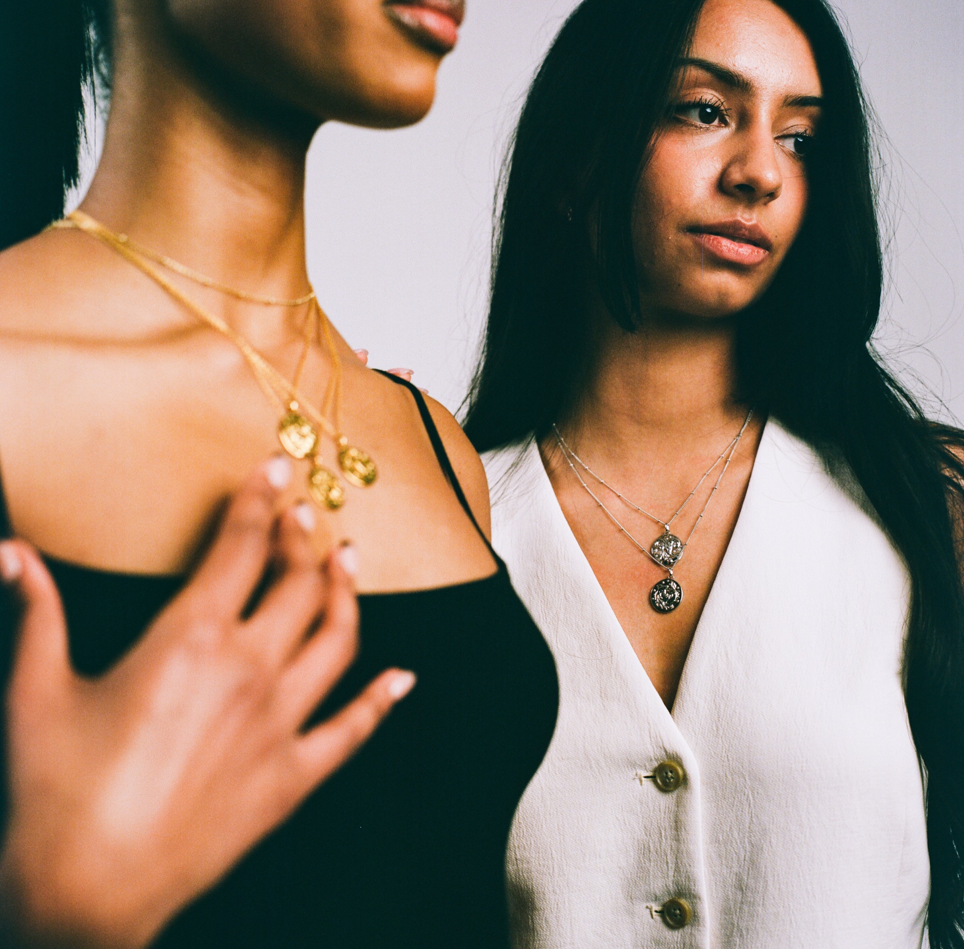 Layered gold zodiac pendants on two models, one resting a hand at her collarbone