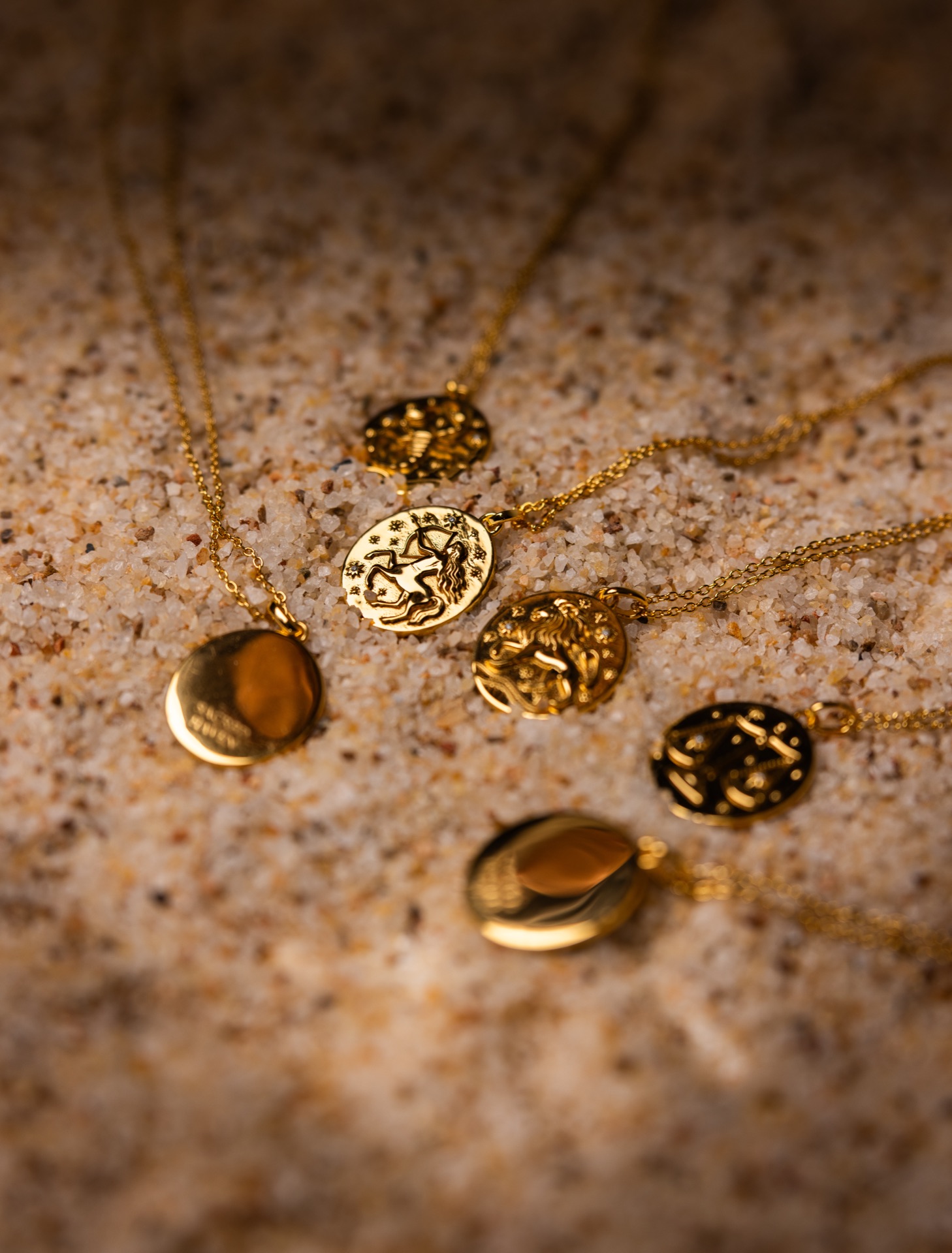 Cluster of gold zodiac pendants and lockets resting on sand