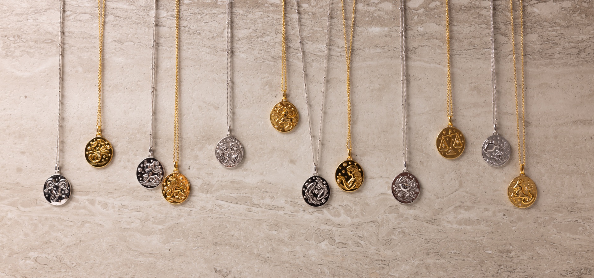 Overhead row of gold and silver zodiac pendants arranged along a travertine slab