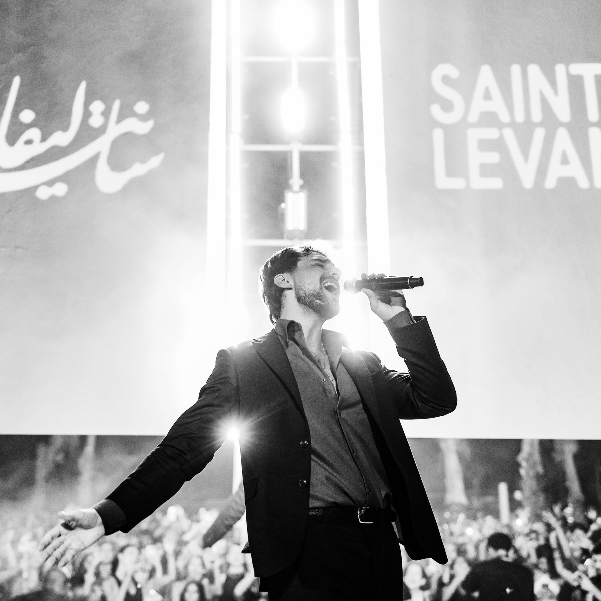Black and white square frame, arms wide against the lit backdrop