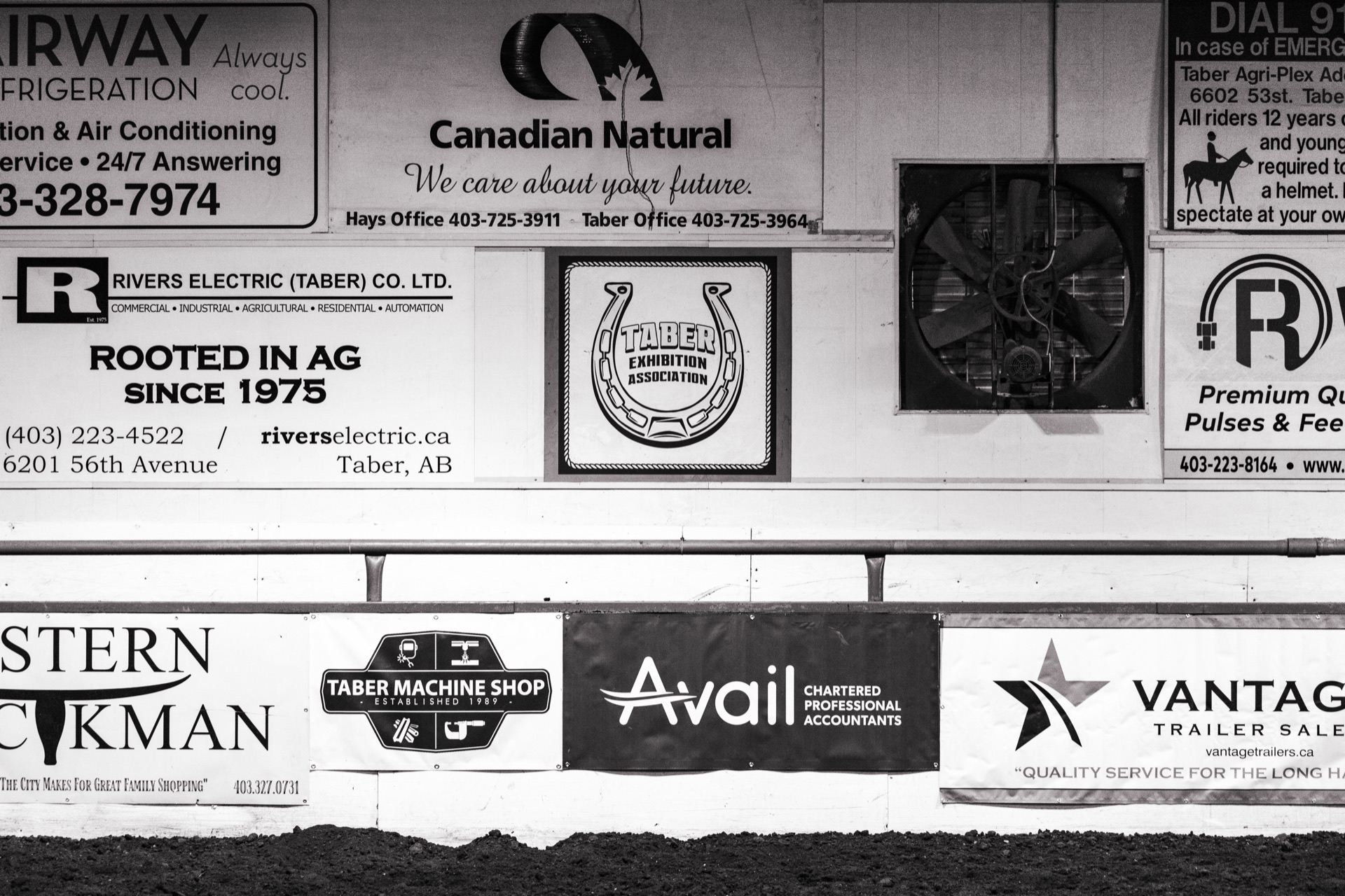 The arena's sponsor boards — local ag, trades and equipment businesses — above the dirt
