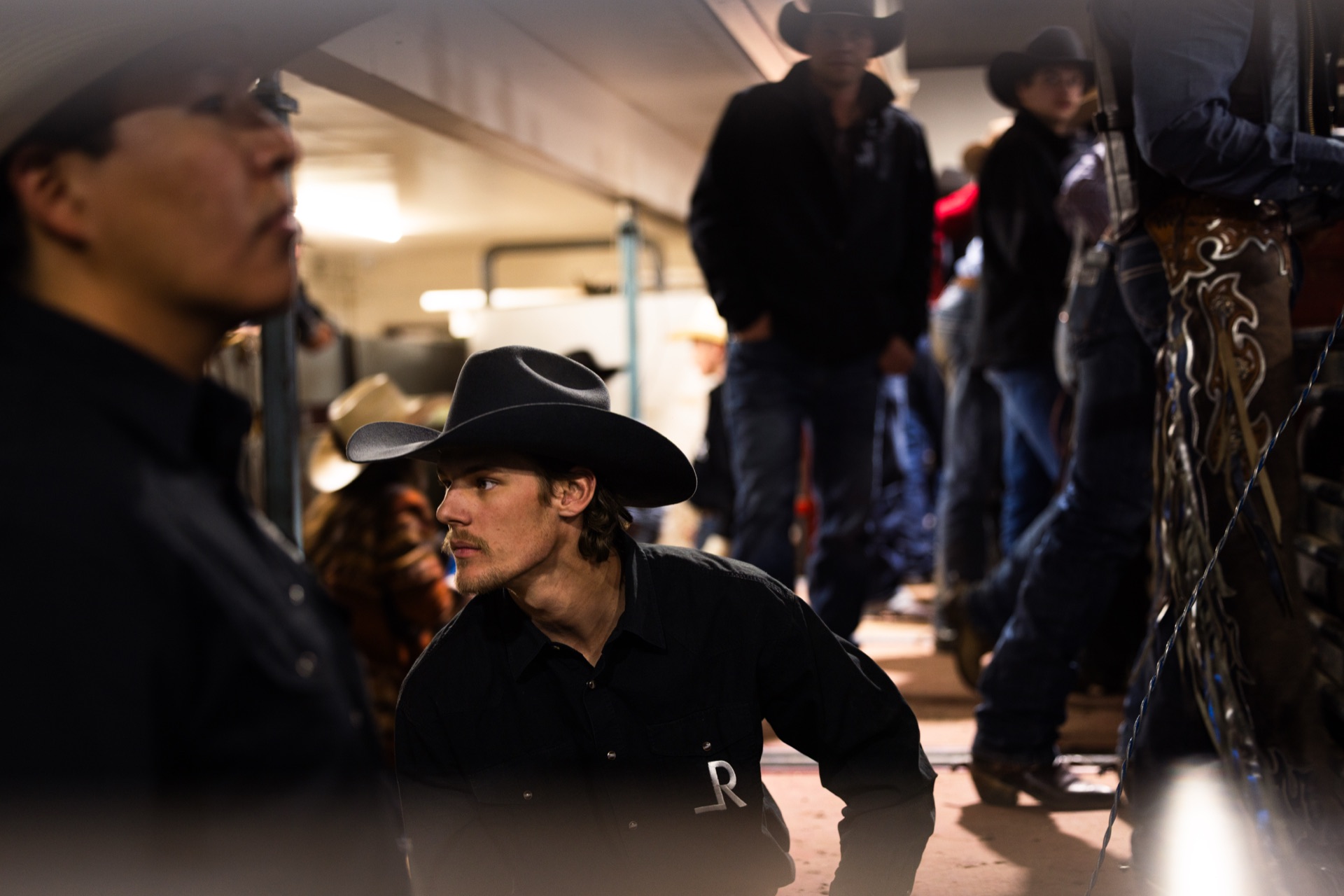A cowboy crouches in the low light of the ready area, others standing around him