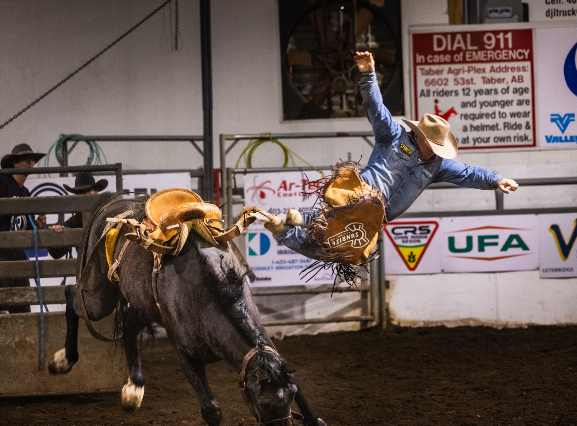 A rider is thrown clear of a bucking horse, an emergency notice board on the wall behind