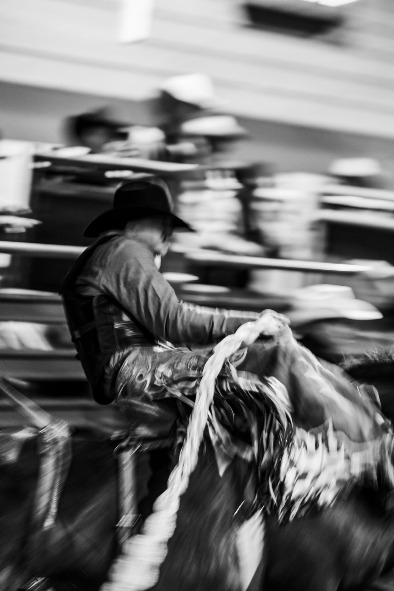 Motion-blurred black and white frame of a rider on a bucking horse in front of the chutes