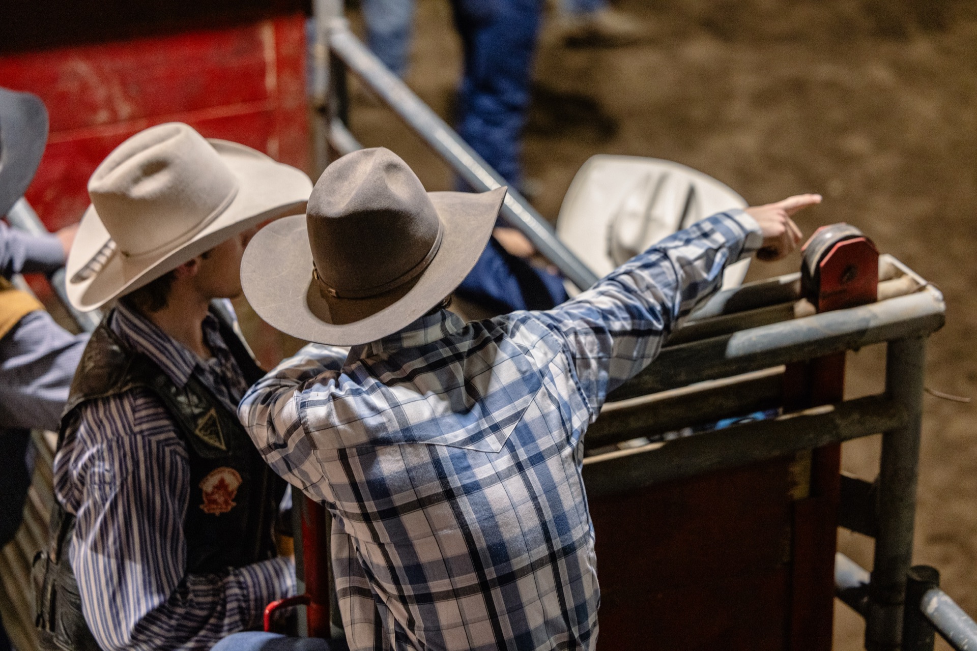 Two men in cowboy hats lean over the chute gate, one reaching for the latch