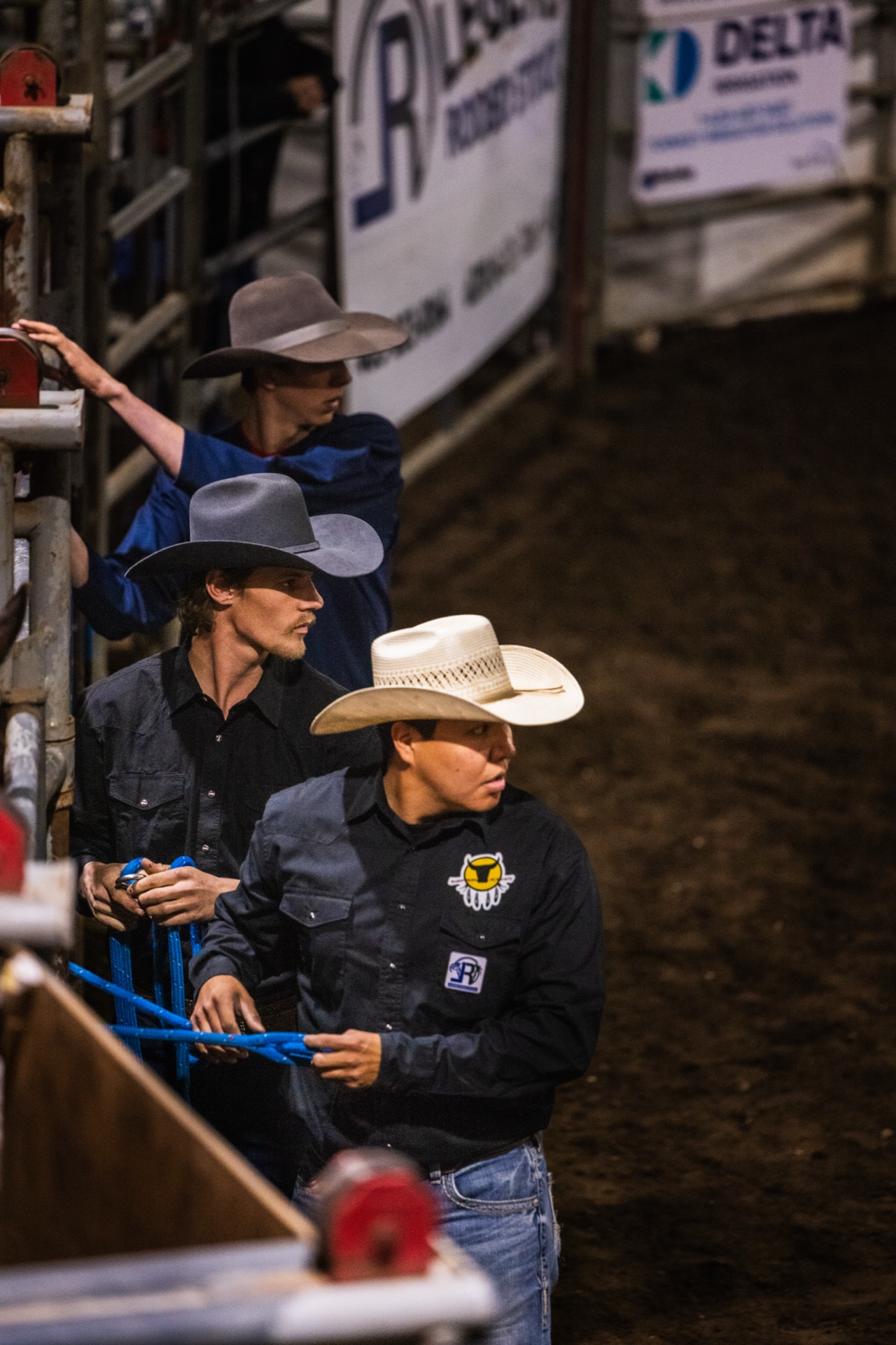 Three men stand behind the chute rail holding a coiled rope, waiting on a run