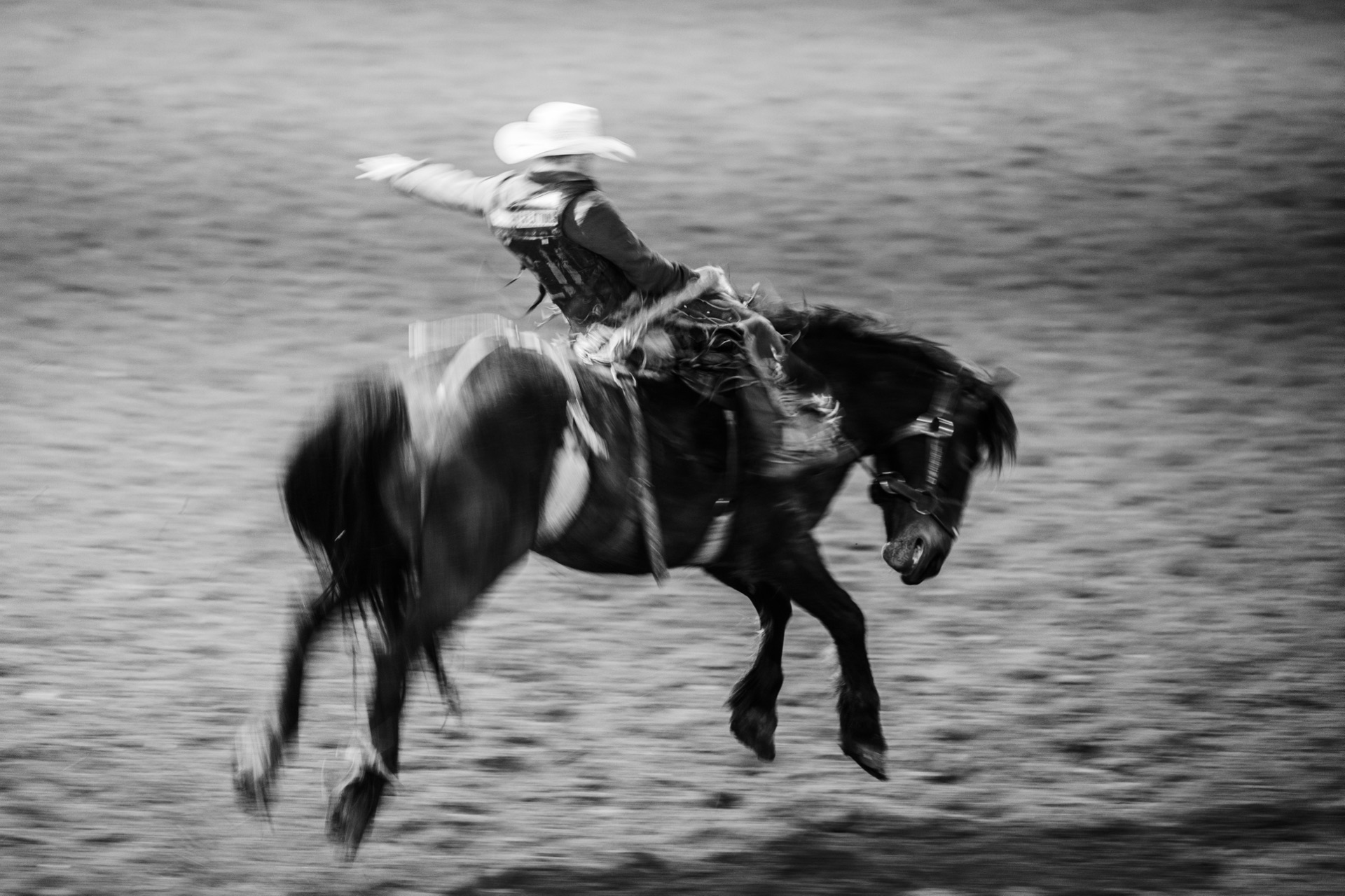 Pan-blurred black and white frame of a rider on a pinto bronc mid-buck