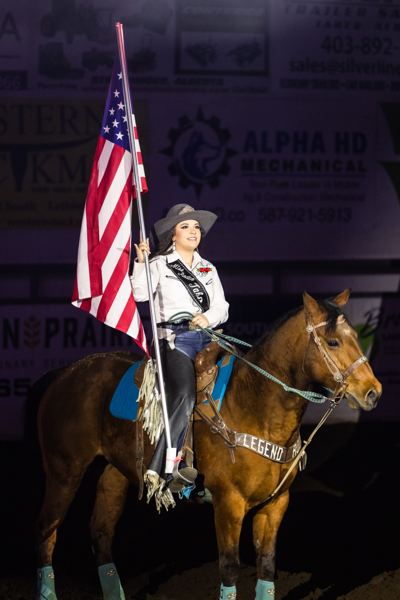A rodeo queen carries the American flag from horseback in the grand entry