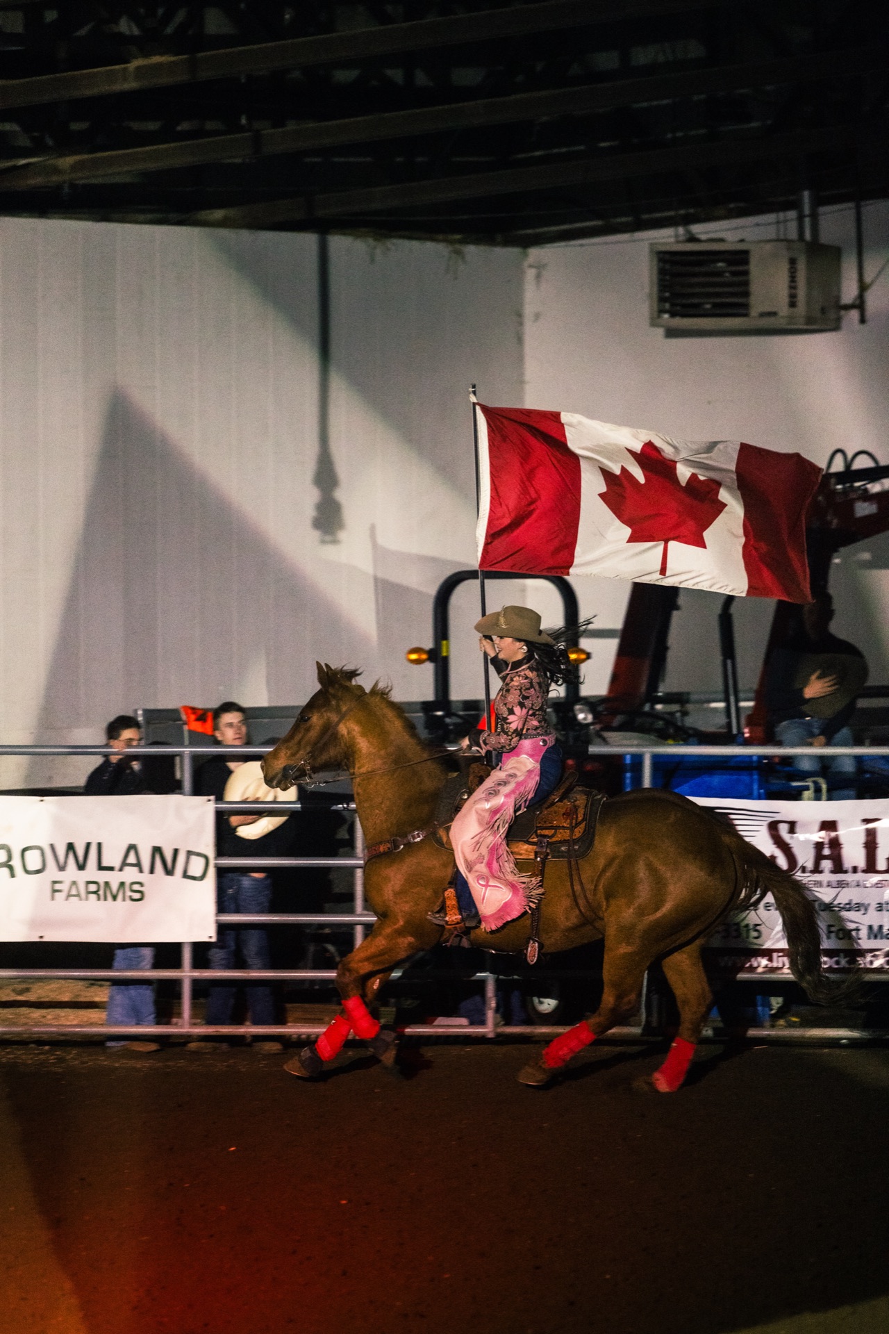 A rider carries the Canadian flag at a gallop past the sponsor boards