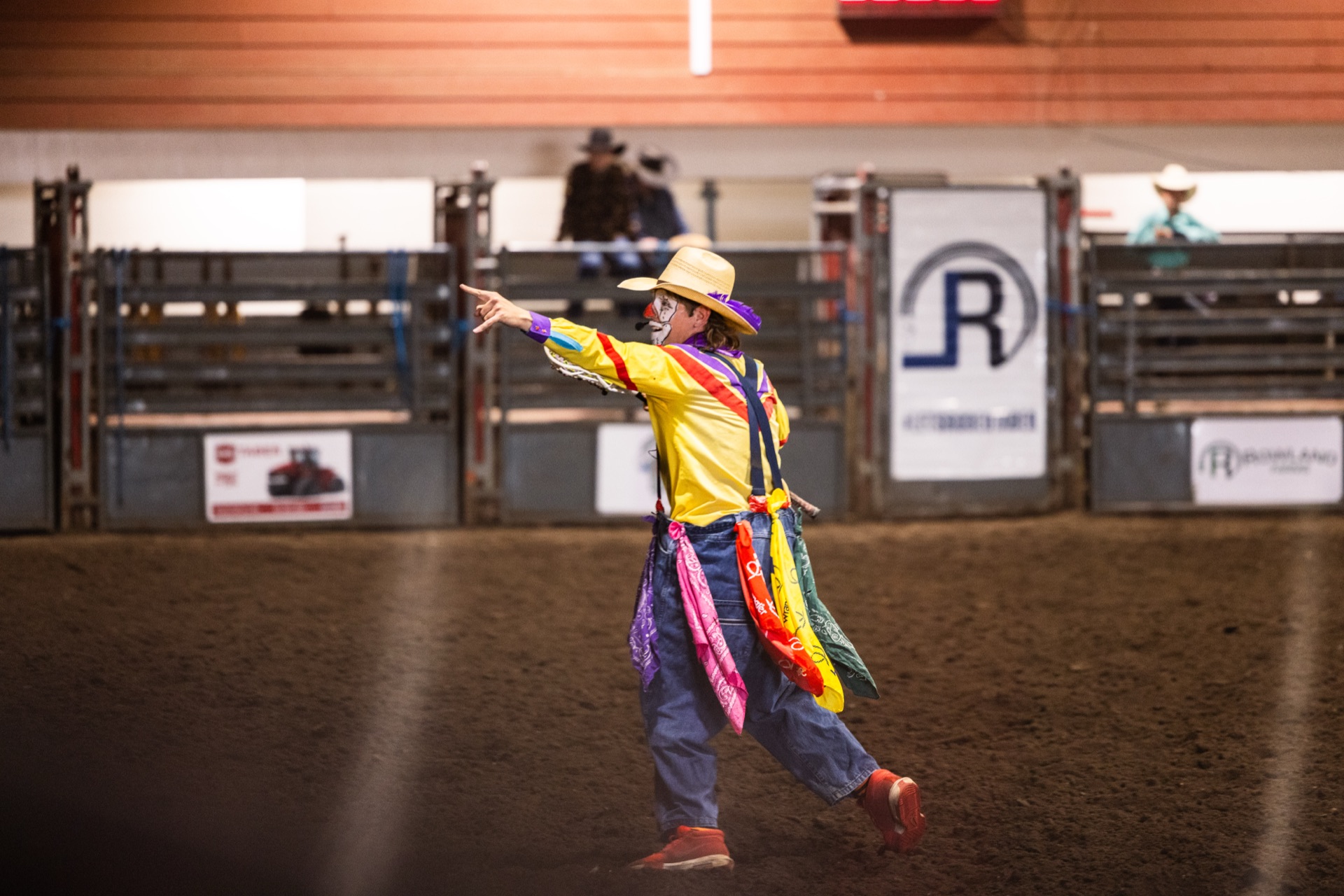 The rodeo clown walking the empty arena, arm outstretched toward the stands