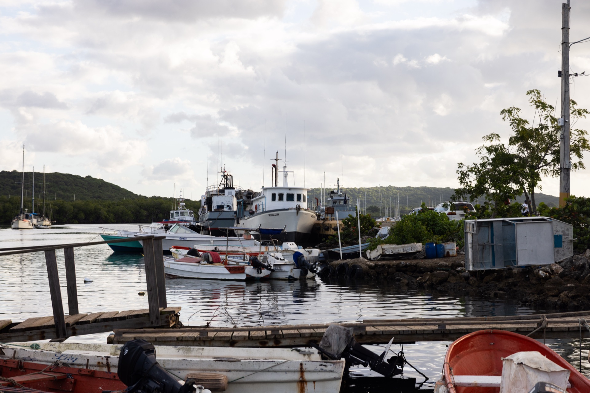 Fishing boats moored along a harbour wall under overcast light, small outboard skiffs in the foreground